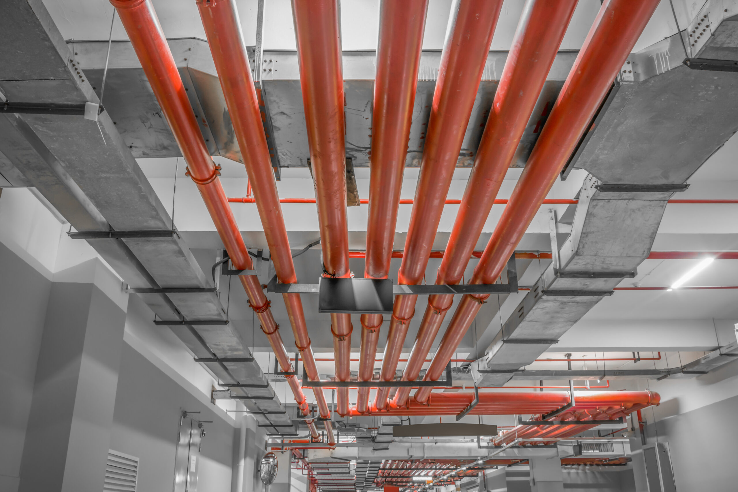 Red fire protection pipework running along the ceiling of a commercial building beside ventilation ducts