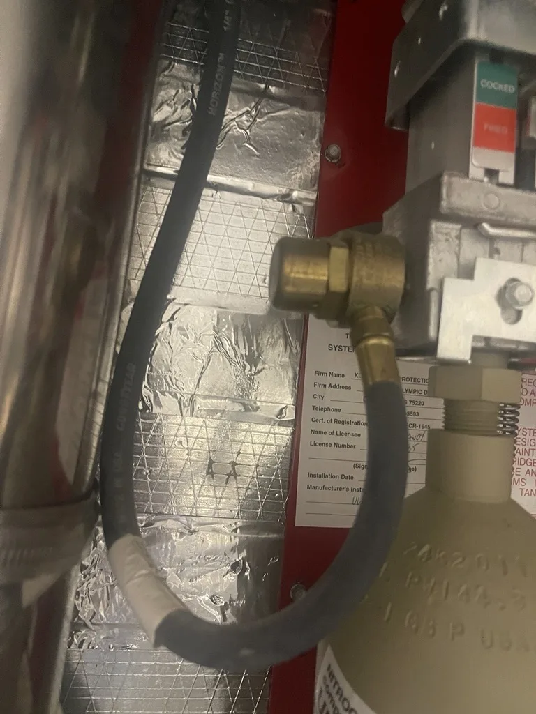 Boss Fire Protection mounting the cylinder, control head, and actuation hardware on a kitchen fire suppression system in Dallas-Fort Worth, TX