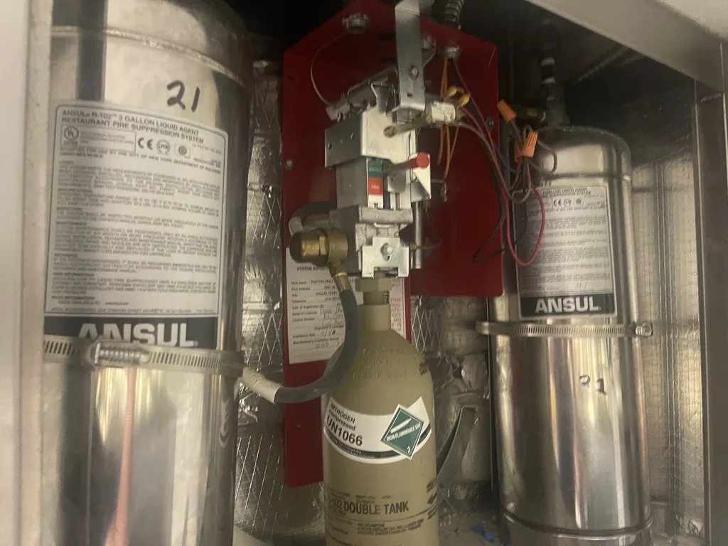 Open ANSUL R-102 fire suppression control head cabinet with two agent tanks during a Boss Fire Protection repair in Dallas-Fort Worth, TX