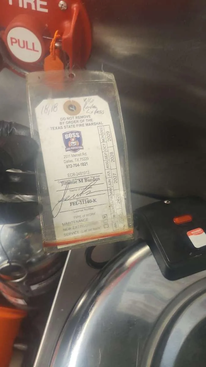 A current Boss Fire Protection service tag re-applied to a commercial kitchen fire suppression pull station after a repair near DFW Airport, TX