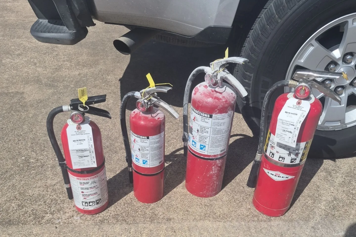 Four used fire extinguishers lined up on pavement beside a service truck on a Boss Fire Protection job.